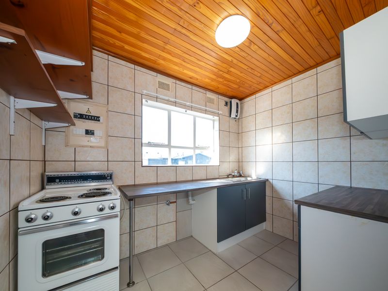 A functional kitchen featuring tiled walls and flooring, a timber ceiling, built-in cabinetry with laminate countertops, and an electric stove.