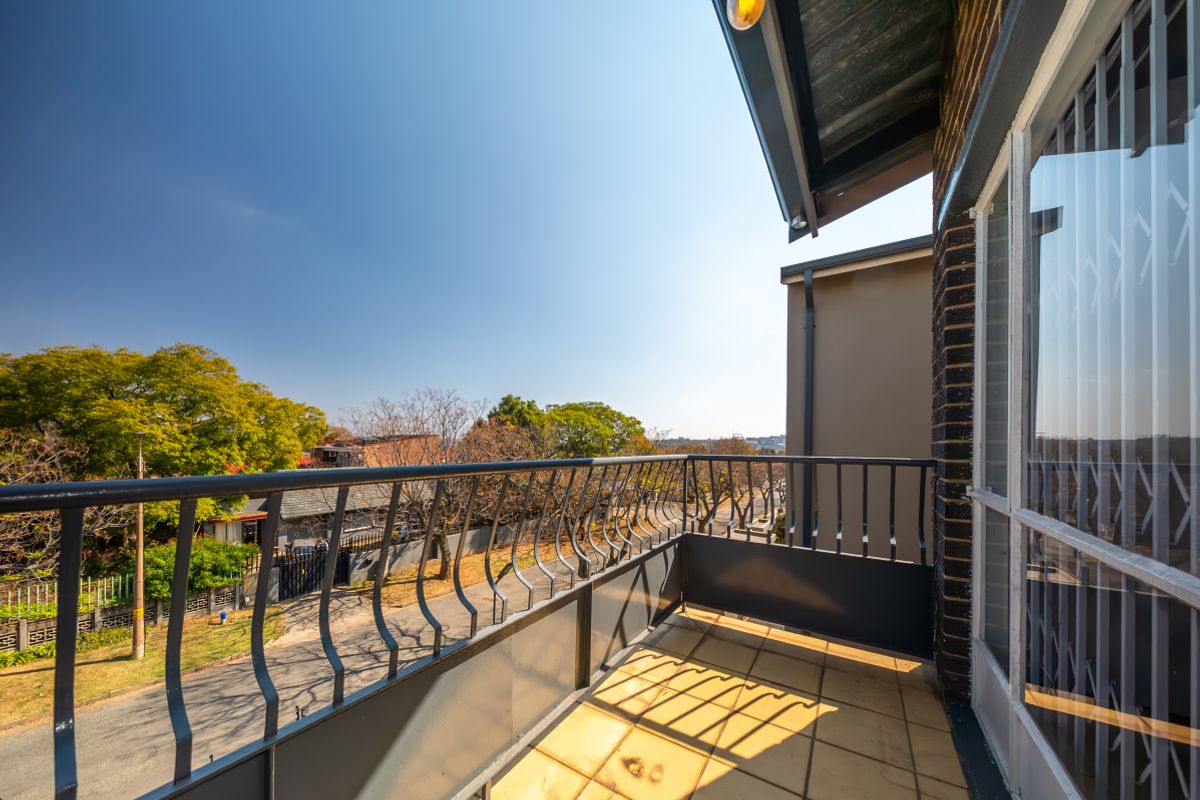 A clean, open-air balcony featuring a metal balustrade, tiled flooring, and a security gate, offering an elevated view of the surrounding neighborhood.
