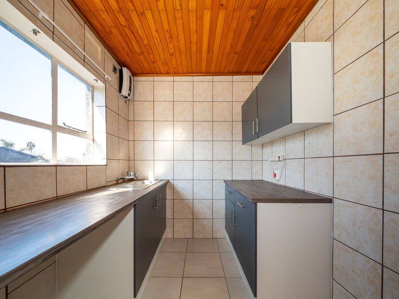 A functional kitchen featuring built-in cabinetry, laminate countertops, a stainless steel sink, and tiled finishes with a timber ceiling.