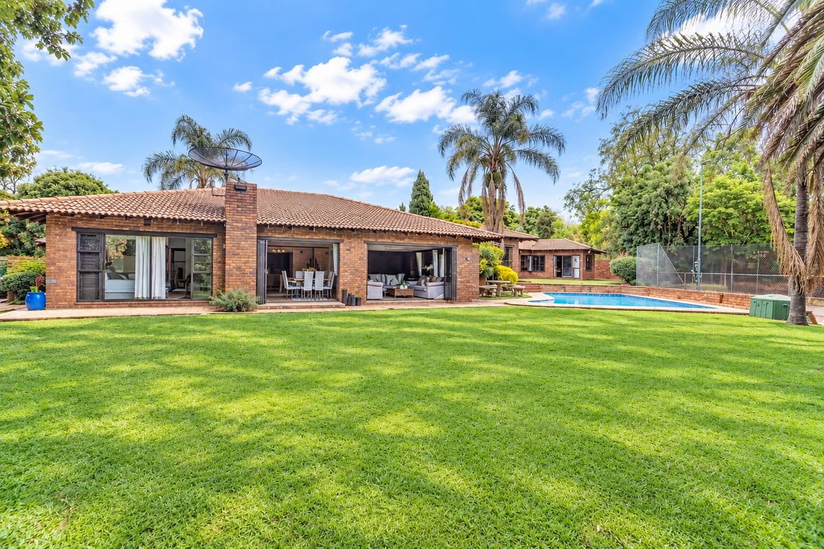 Spacious rear exterior view featuring a well-maintained lawn, swimming pool, and a brick-built home with large sliding doors opening to the garden.