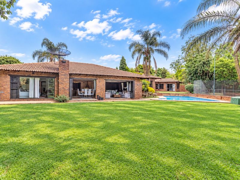Spacious rear exterior view featuring a well-maintained lawn, swimming pool, and a brick-built home with large sliding doors opening to the garden.