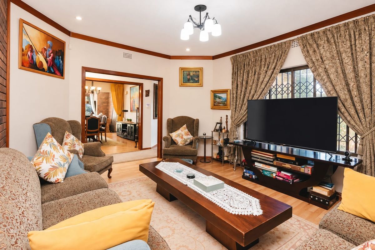 A comfortable living room featuring laminate flooring, coving, and a security gate, with an open-plan flow leading into the adjacent dining area.