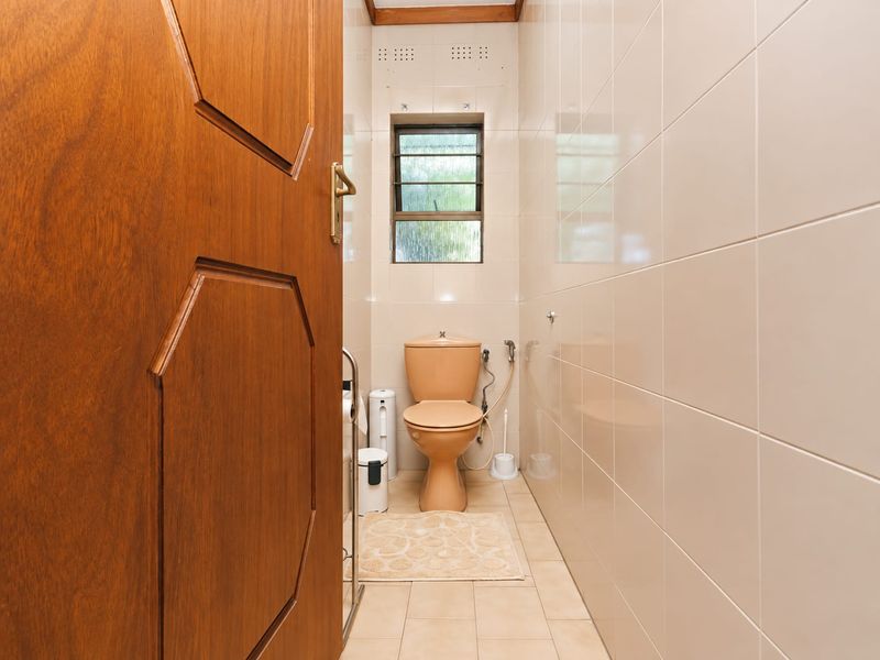 A compact guest bathroom featuring floor-to-ceiling wall tiles, a louver window for ventilation, and a functional toilet suite.