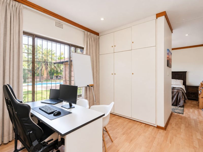 A functional bedroom featuring built-in cupboards, laminate flooring, and large windows with security bars, offering a view of the garden and pool area.
