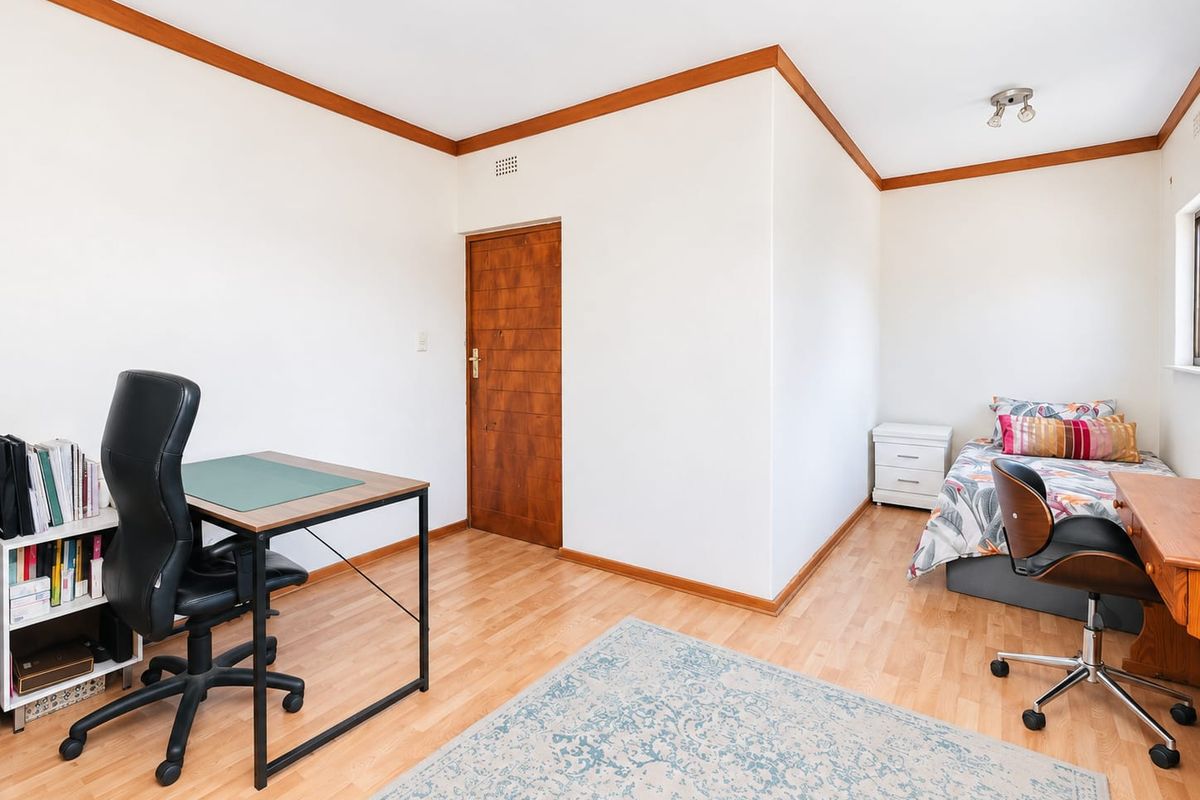 A functional bedroom featuring laminate flooring, timber door, and timber ceiling trim, offering a neutral space ready for personalization.