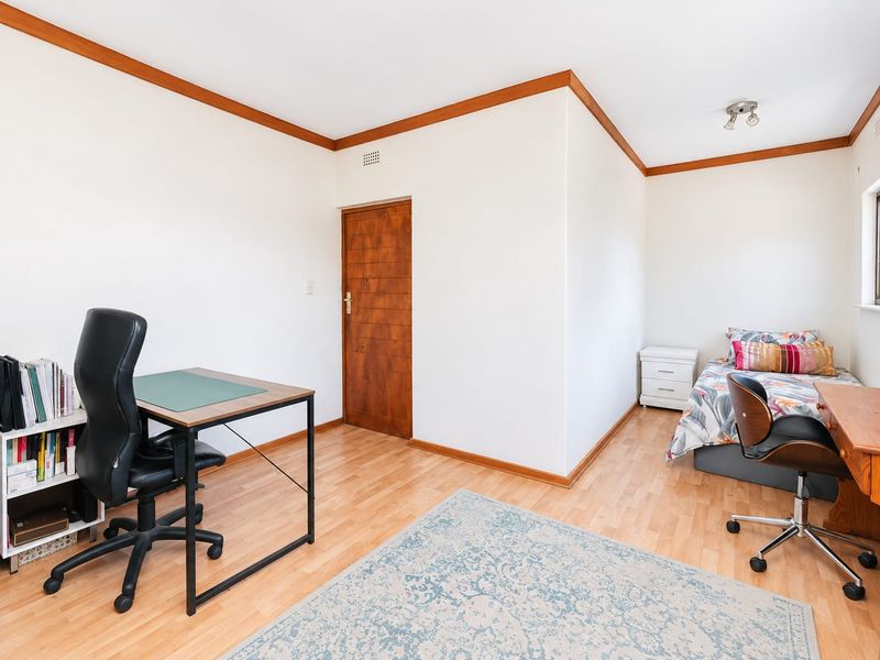 A functional bedroom featuring laminate flooring, timber door, and timber ceiling trim, offering a neutral space ready for personalization.