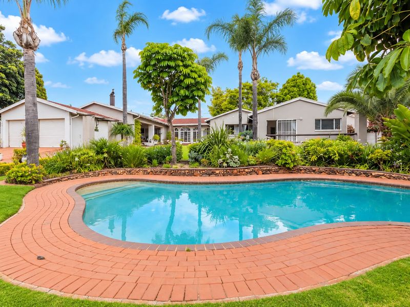 A well-maintained backyard featuring a swimming pool with brick paving, stone retaining walls, and established garden landscaping.
