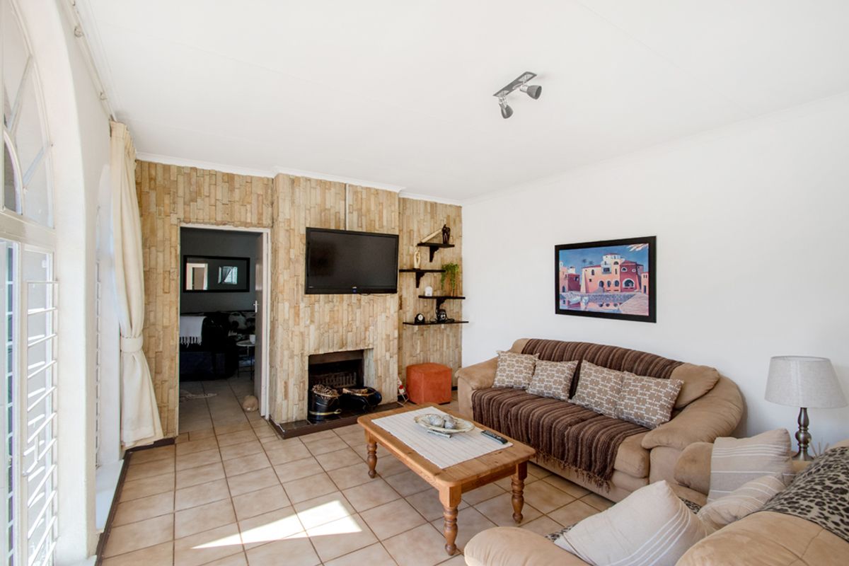 A comfortable living room featuring a prominent stone-clad fireplace, tiled flooring, and an arched window that allows for natural light.