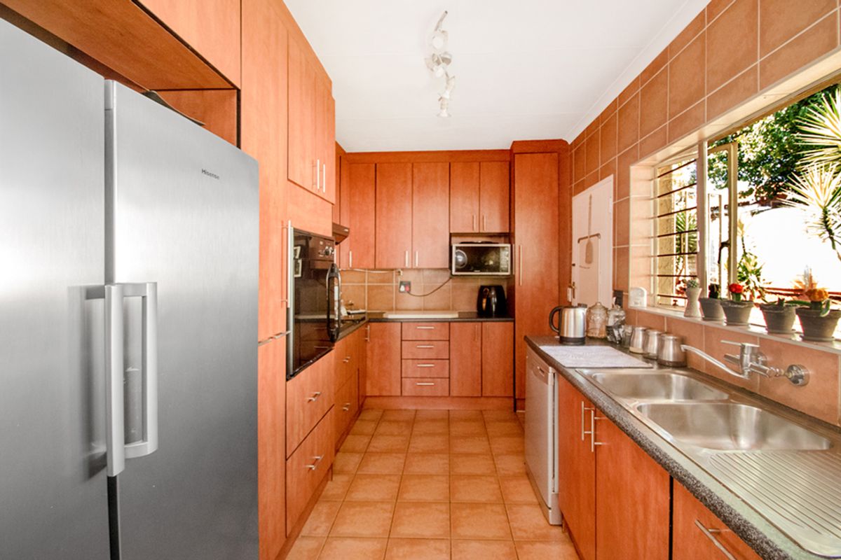 A functional kitchen featuring warm-toned wooden cabinetry, tiled backsplash, laminate countertops, and a double stainless steel sink with ample storage space.