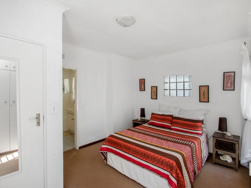 A functional bedroom featuring carpeted flooring, built-in cupboards, a unique glass block window, and direct access to an en-suite bathroom.