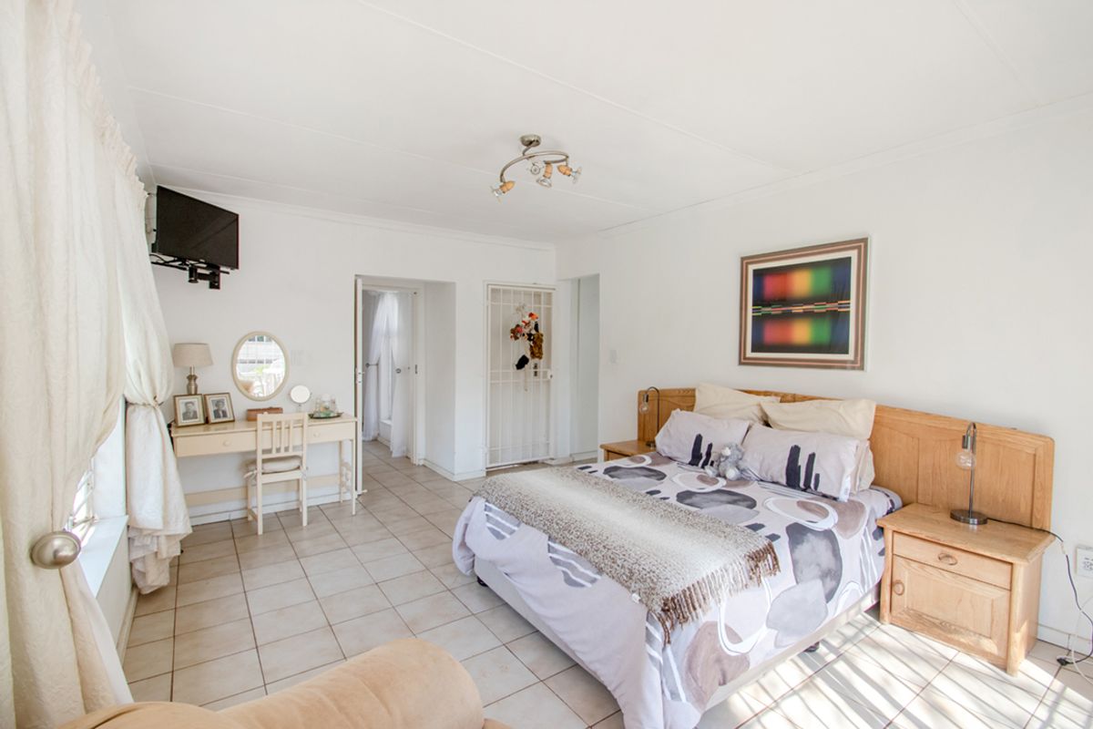 A spacious bedroom featuring tiled flooring, a built-in wooden headboard, and a security gate leading to an adjacent area.