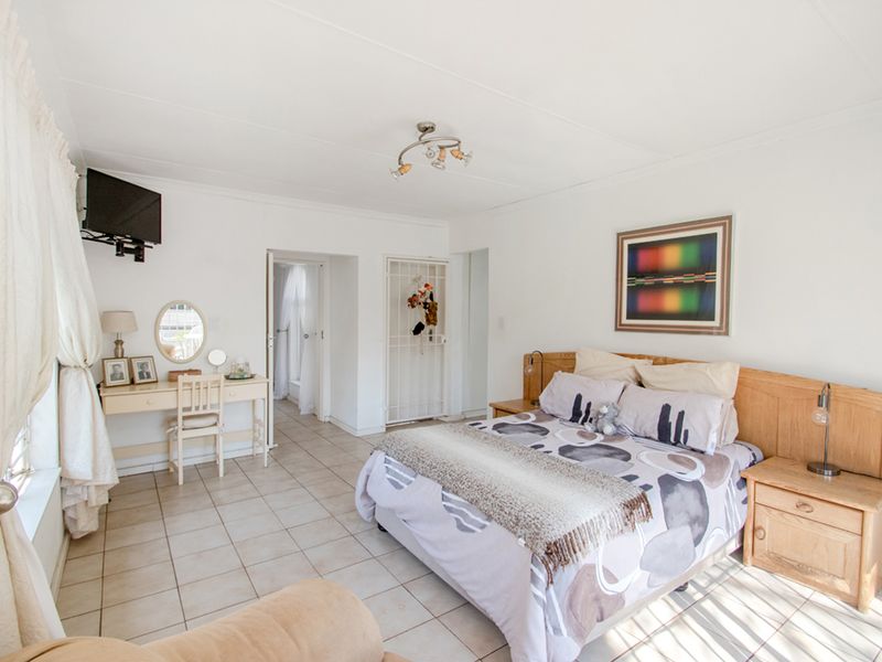 A spacious bedroom featuring tiled flooring, a built-in wooden headboard, and a security gate leading to an adjacent area.