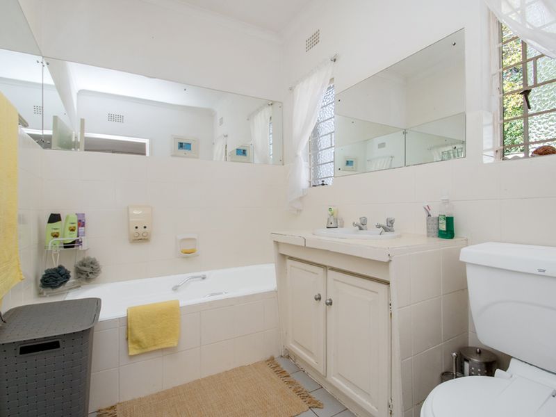 A functional bathroom featuring a tiled bathtub, built-in vanity with basin, and wall-mounted mirrors, offering a classic layout with potential for modern updates.