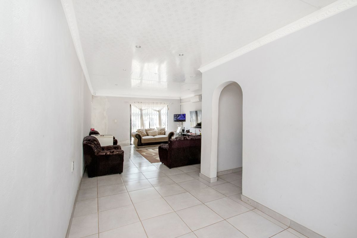 A living room featuring tiled flooring, an arched entryway, and recessed ceiling lighting, with visible wall surface imperfections requiring repair.