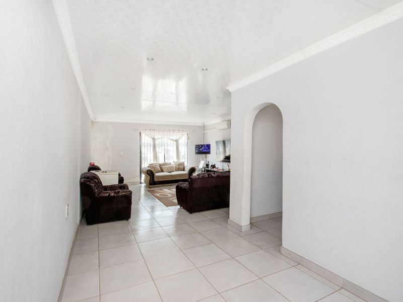 A living room featuring tiled flooring, an arched entryway, and recessed ceiling lighting, with visible wall surface imperfections requiring repair.
