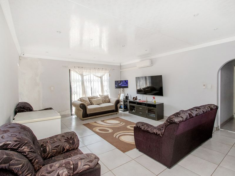 Spacious living room featuring tiled flooring, recessed lighting, and a wall-mounted air conditioning unit, with some visible wall surface repairs required.