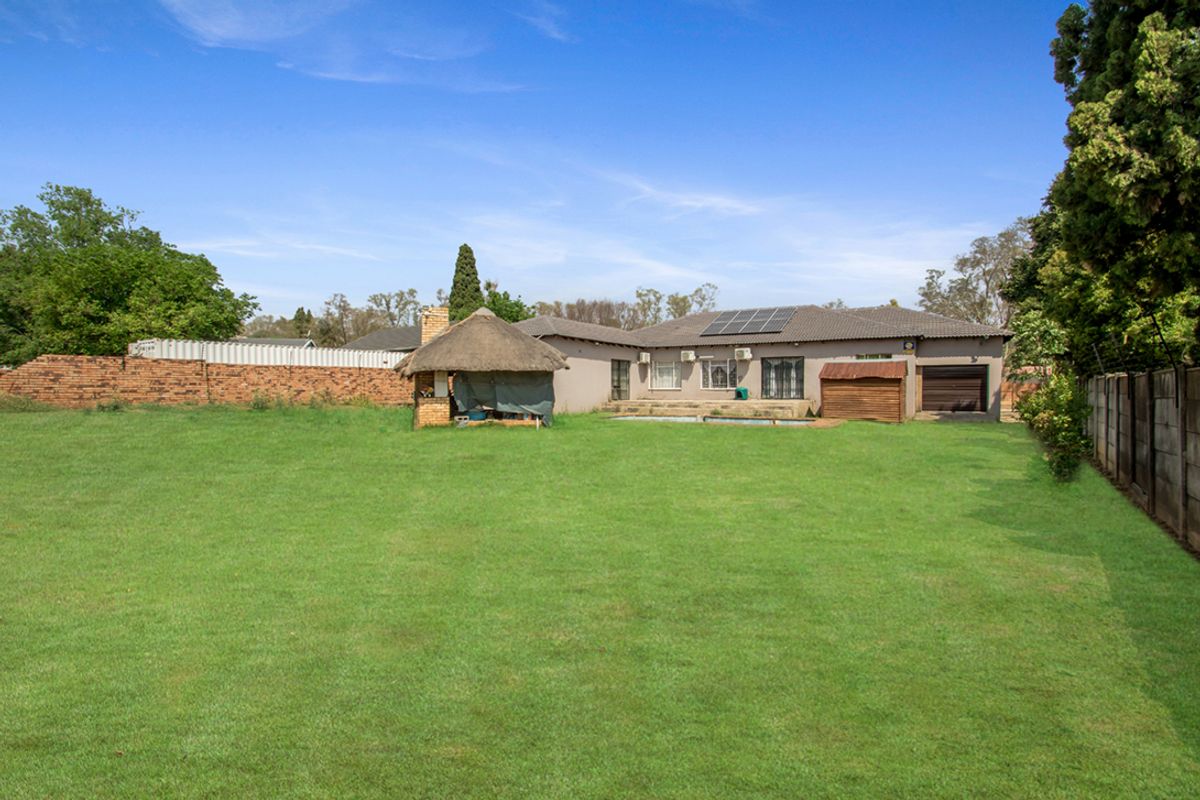 Spacious rear garden featuring a large lawn, swimming pool, and a traditional thatched lapa, with direct access to the main house and garage.