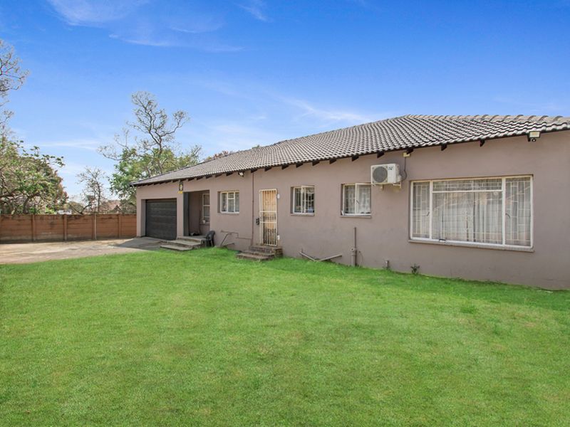 Rear view of the property featuring a large lawn, concrete driveway, garage access, and exterior wall with an installed air conditioning unit.