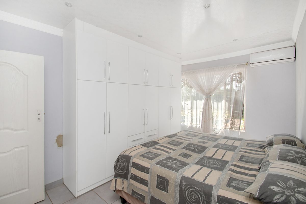 A bedroom featuring white built-in cupboards, tiled flooring, recessed lighting, and a wall-mounted air conditioning unit.