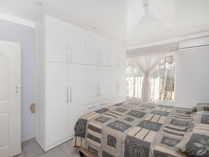 A bedroom featuring white built-in cupboards, tiled flooring, recessed lighting, and a wall-mounted air conditioning unit.
