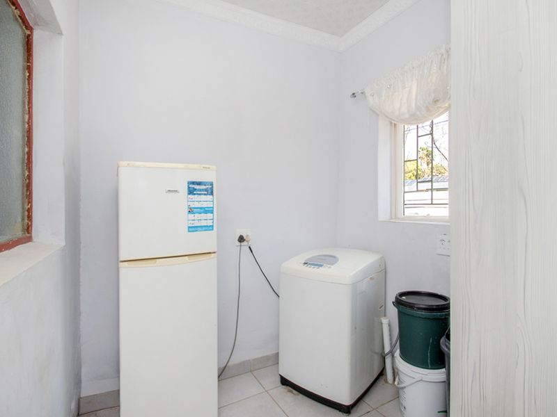 A functional laundry area featuring tiled flooring and security bars on the window, providing a practical space for utility and washing appliances.