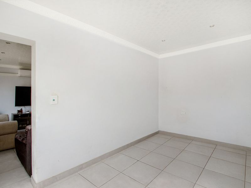 A bright, empty living area featuring neutral tiled flooring, recessed downlighting, and decorative ceiling cornicing, offering a clean canvas for interior design.