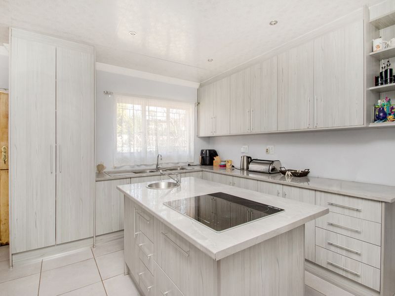 Modern kitchen featuring light wood-grain cabinetry, a central island with an integrated induction hob, tiled flooring, and ample storage space.