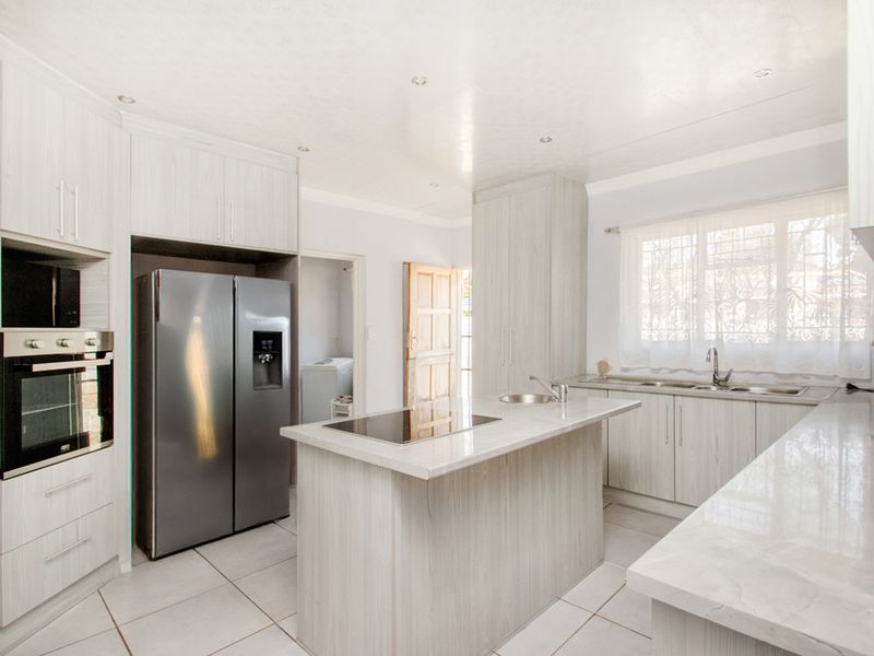 A modern, well-lit kitchen featuring light wood-grain cabinetry, stone countertops, a central island with an integrated cooktop, and a built-in oven.