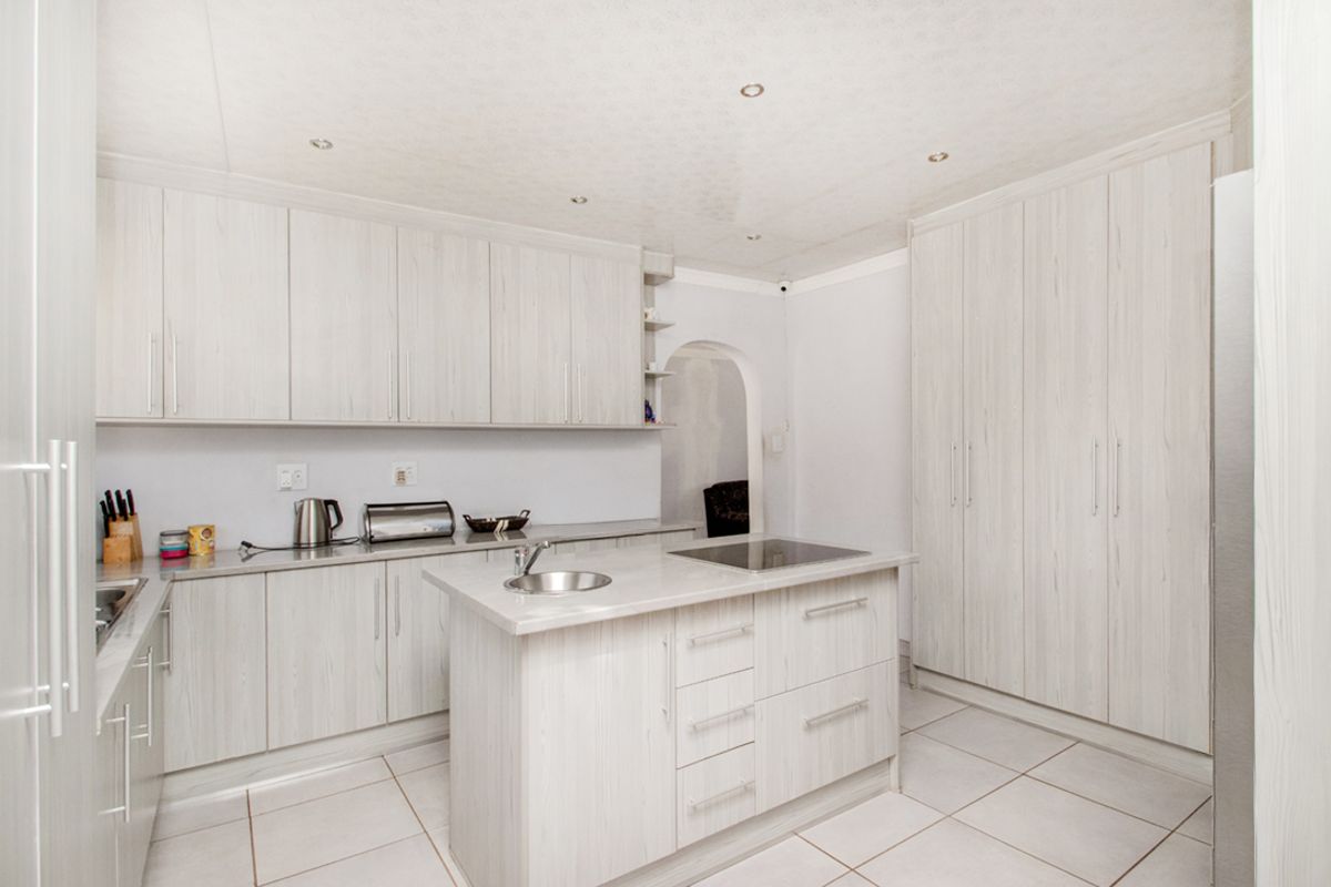 A modern kitchen featuring light wood-grain cabinetry, a central island with a built-in hob and sink, and neutral tiled flooring.