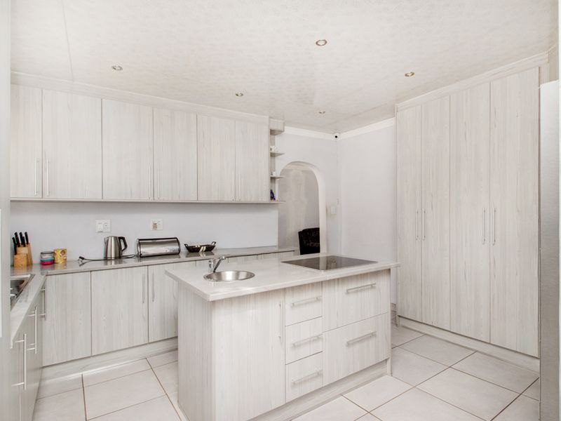 A modern kitchen featuring light wood-grain cabinetry, a central island with a built-in hob and sink, and neutral tiled flooring.