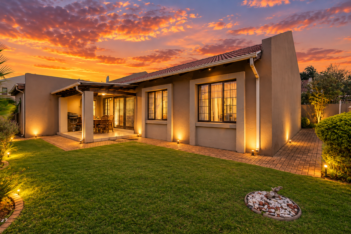 A beautifully presented rear exterior view of the home featuring a covered patio, well-maintained garden, and ambient exterior lighting at sunset.