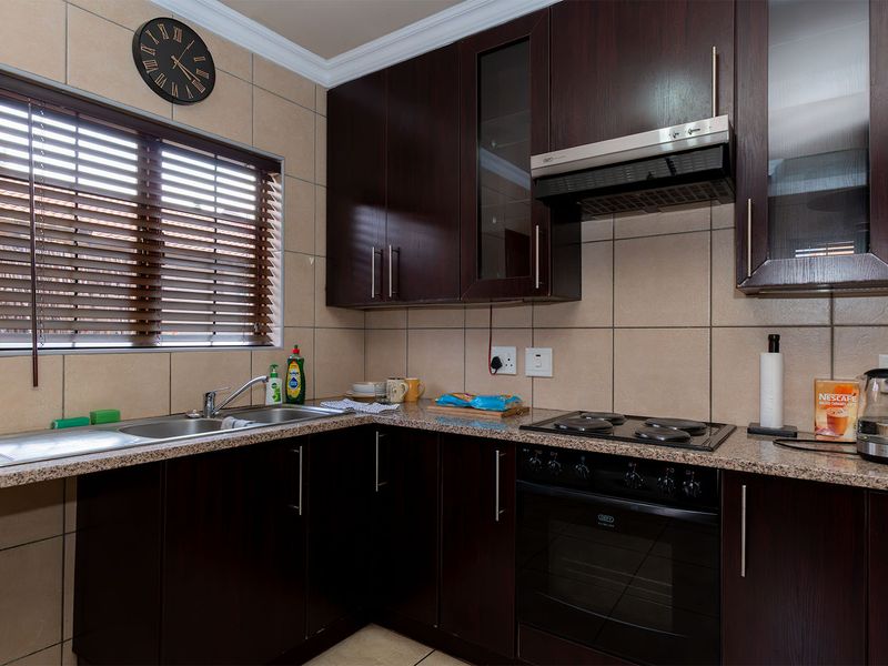 A functional kitchen featuring dark wood cabinetry, granite countertops, a built-in oven with hob, and a stainless steel double sink with tiled backsplash.