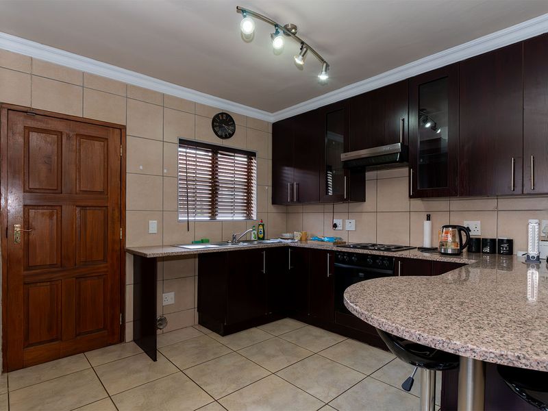 A functional kitchen featuring dark wood cabinetry, granite countertops, a breakfast bar, built-in oven, gas hob, and tiled finishes throughout.