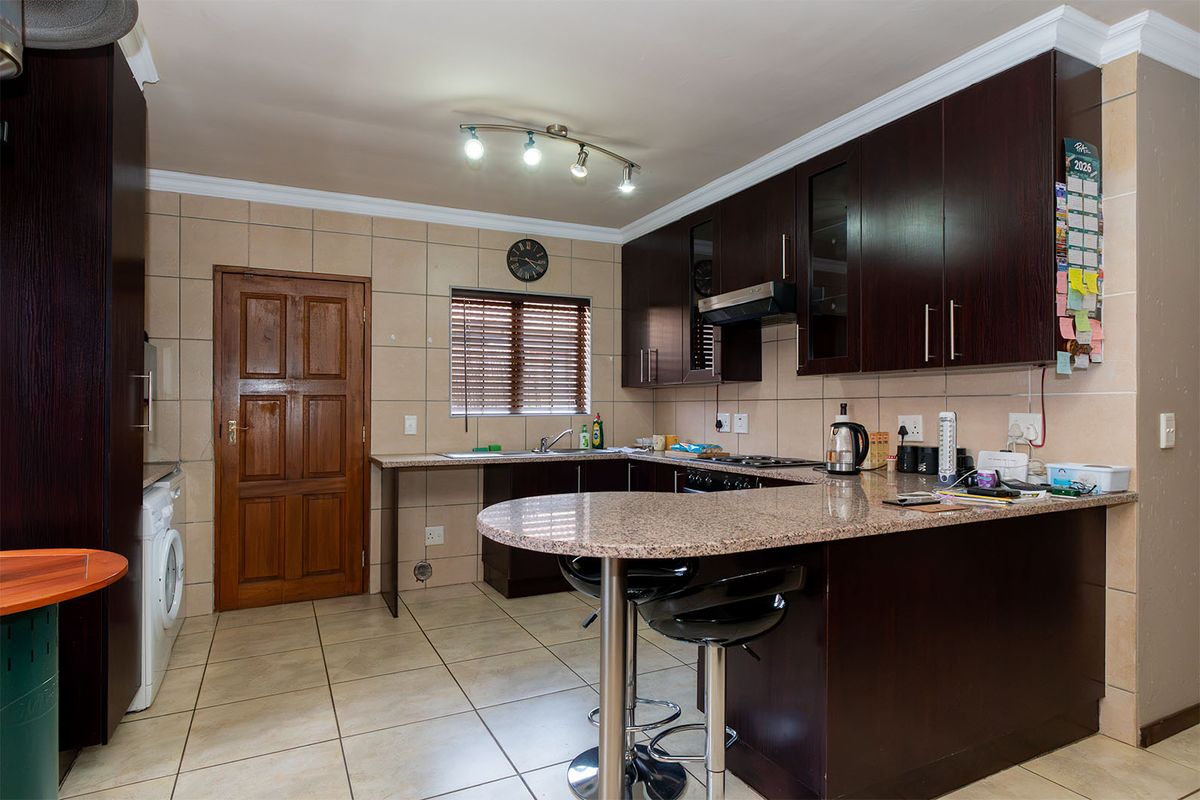 A functional kitchen featuring dark wood cabinetry, granite countertops, a breakfast bar, and tiled flooring with a neutral backsplash.