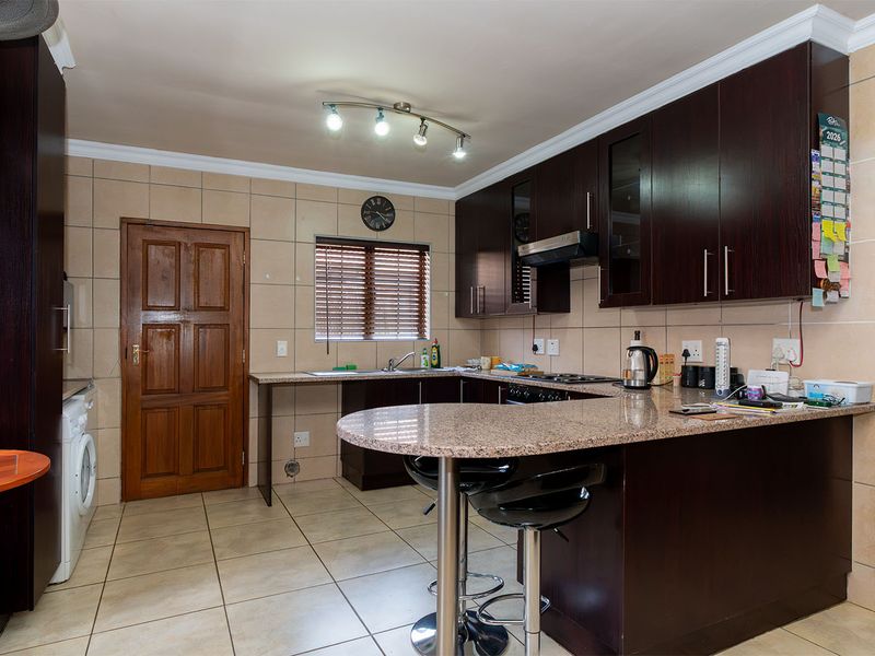 A functional kitchen featuring dark wood cabinetry, granite countertops, a breakfast bar, and tiled flooring with a neutral backsplash.