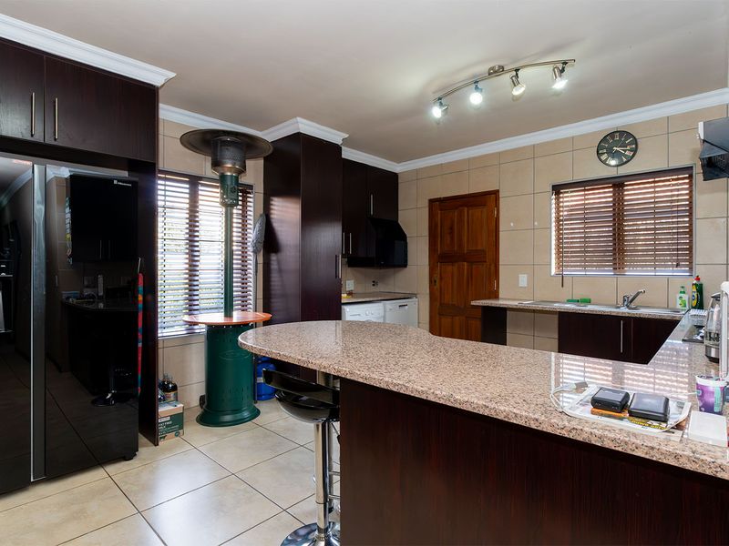 Spacious kitchen featuring dark wood cabinetry, granite countertops, tiled backsplash, and functional track lighting, offering a practical and well-maintained workspace.