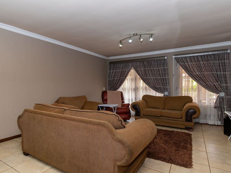 A spacious living room featuring tiled flooring, ceiling coving, and track lighting, offering a neutral base for potential interior updates.