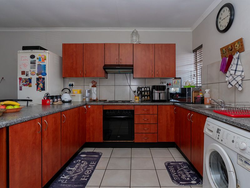 A functional U-shaped kitchen featuring wood-finish cabinetry, granite-look countertops, tiled backsplash, and integrated space for a washing machine.