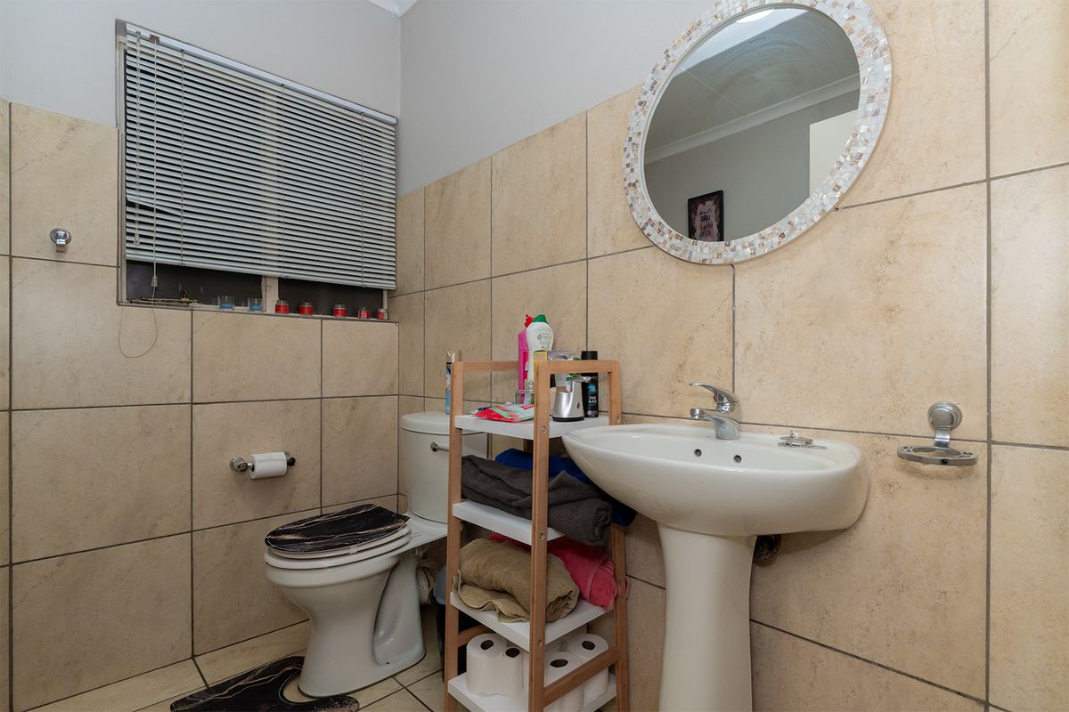 A functional bathroom featuring a pedestal basin, toilet, and neutral ceramic wall and floor tiling with a window blind.