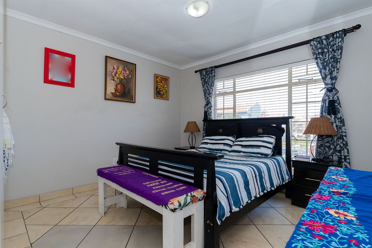 A well-lit bedroom featuring tiled flooring, a large window with venetian blinds, and neutral wall finishes.