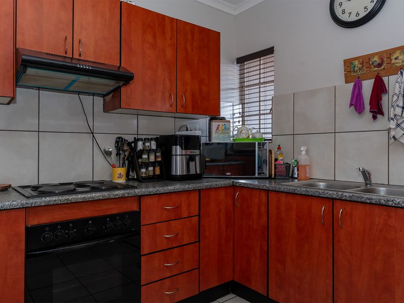 A functional kitchen featuring warm-toned laminate cabinetry, granite countertops, a built-in electric oven and hob, and a tiled backsplash.