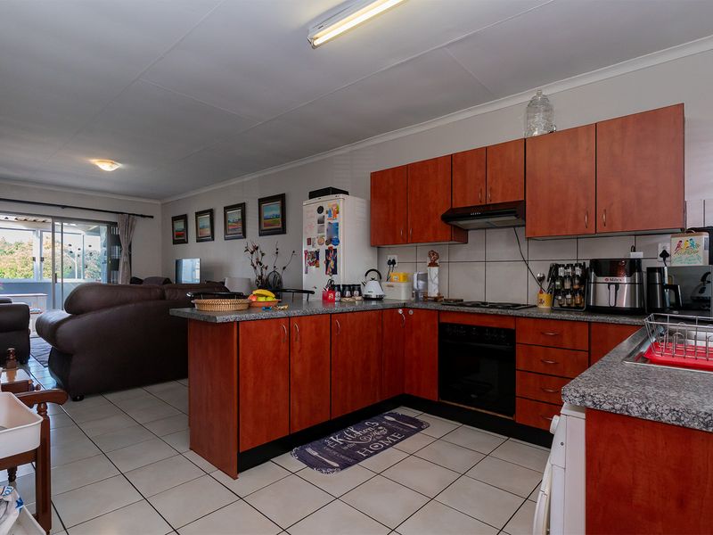 Open-plan kitchen and living area featuring wood-finish cabinetry, granite countertops, built-in appliances, and tiled flooring with access to a patio.