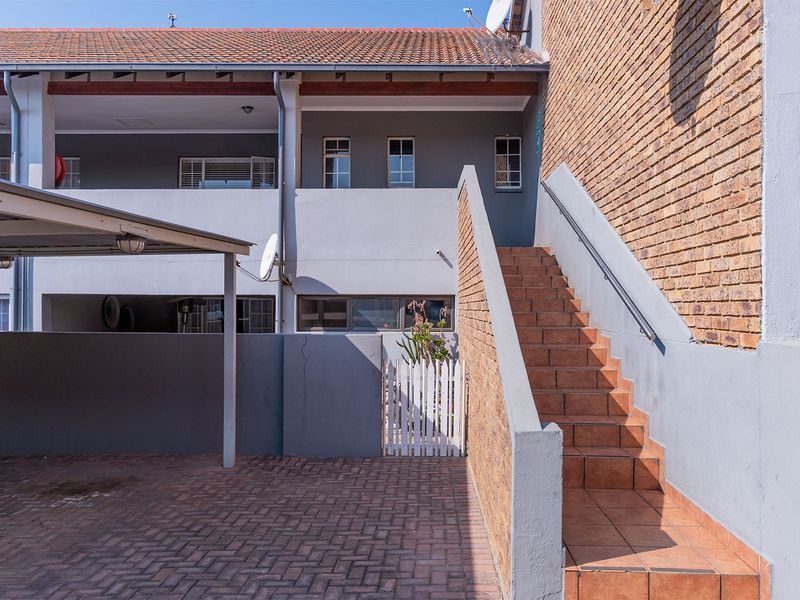 Exterior view of the apartment complex featuring a paved driveway, covered carport, and a tiled staircase leading to the upper level units.