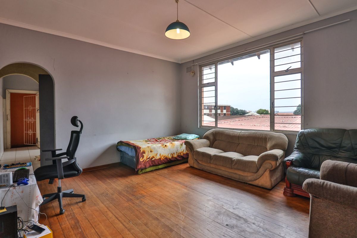 A spacious bedroom featuring original hardwood flooring, large windows providing natural light, and an arched entryway leading to an adjacent area.