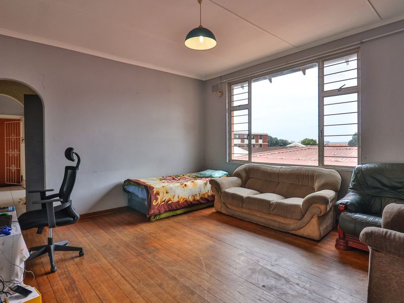 A spacious bedroom featuring original hardwood flooring, large windows providing natural light, and an arched entryway leading to an adjacent area.