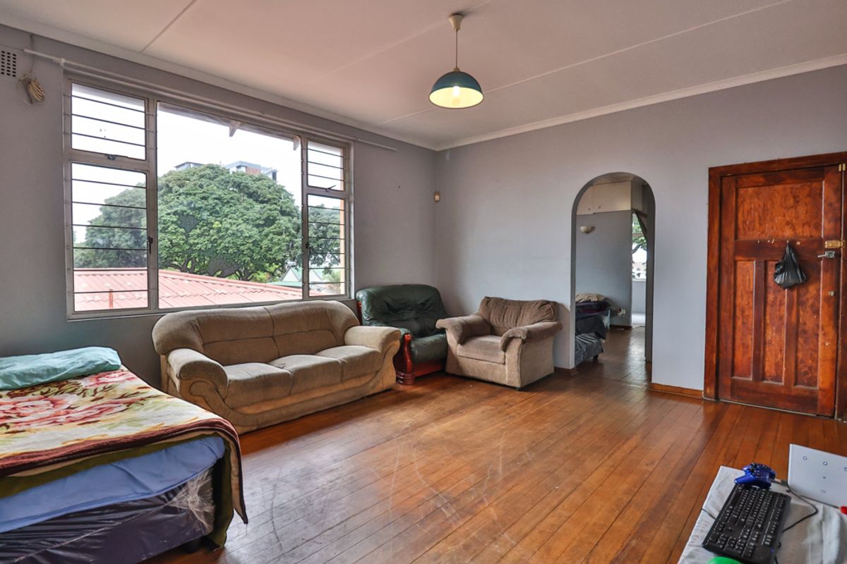 Spacious living room featuring original hardwood flooring, an arched entryway, and large windows providing natural light and an elevated outlook.