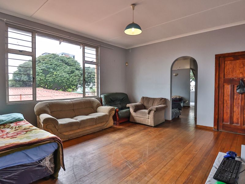 Spacious living room featuring original hardwood flooring, an arched entryway, and large windows providing natural light and an elevated outlook.