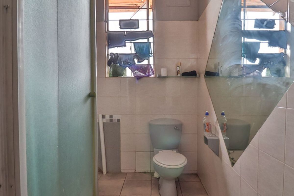 A functional bathroom featuring a toilet, shower enclosure, and tiled finishes, currently requiring cosmetic updates and maintenance to improve its overall condition.