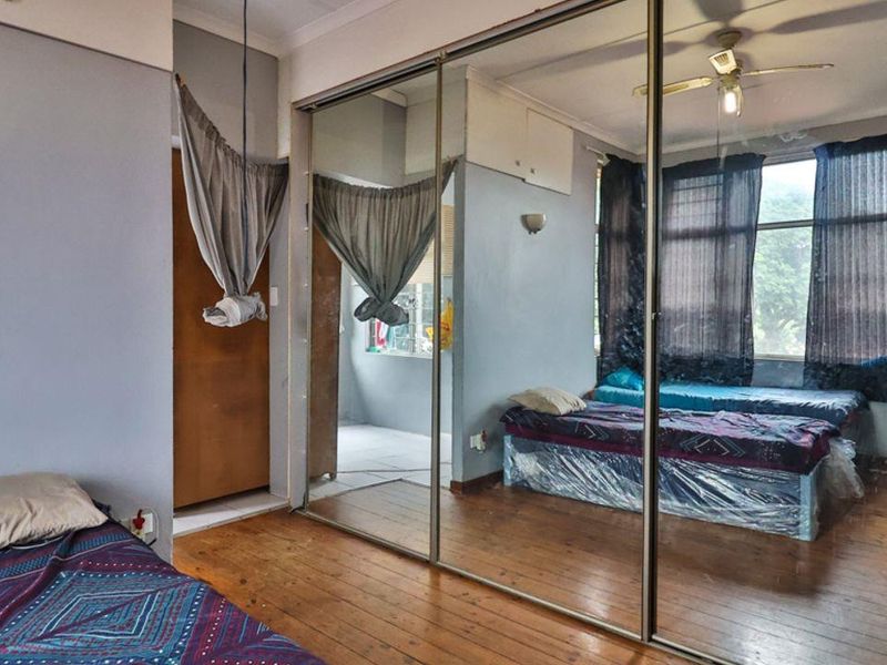 A bedroom featuring hardwood flooring, a large built-in mirrored wardrobe, and a ceiling fan, offering a functional space with potential for cosmetic updates.