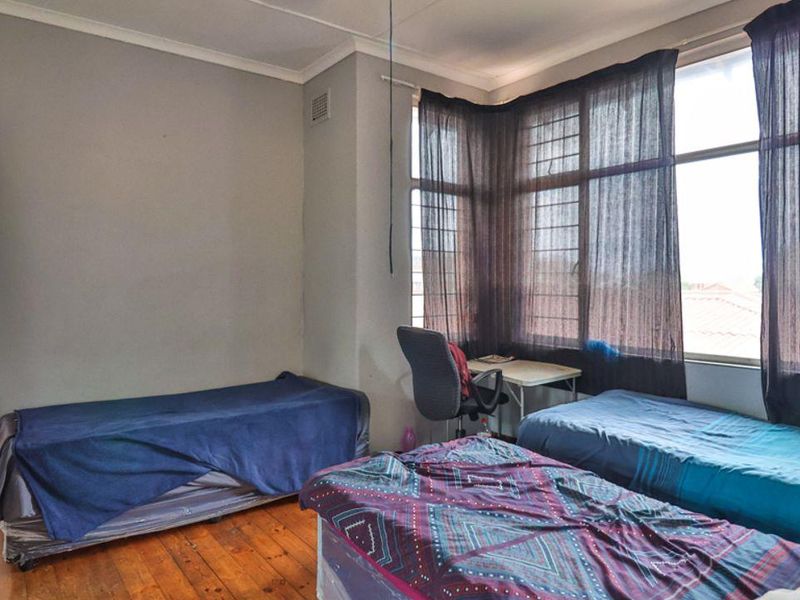 A bedroom featuring original timber flooring, large windows with security bars, and coved cornicing, offering a functional space with potential for cosmetic updates.